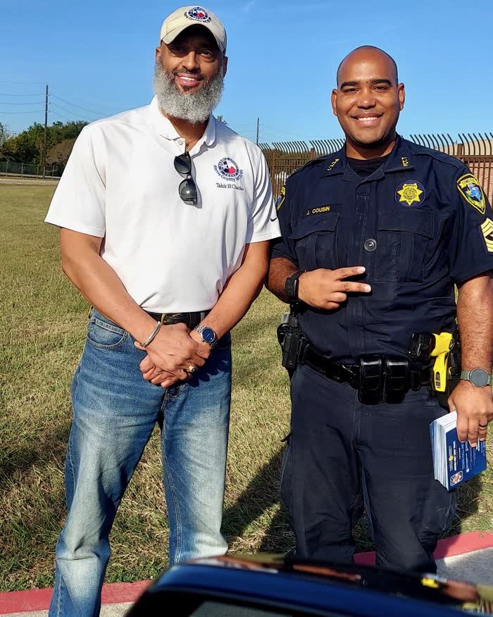 Tahir Charles standing beside a Harris County constable deputy holding a stack of blue leaflets.