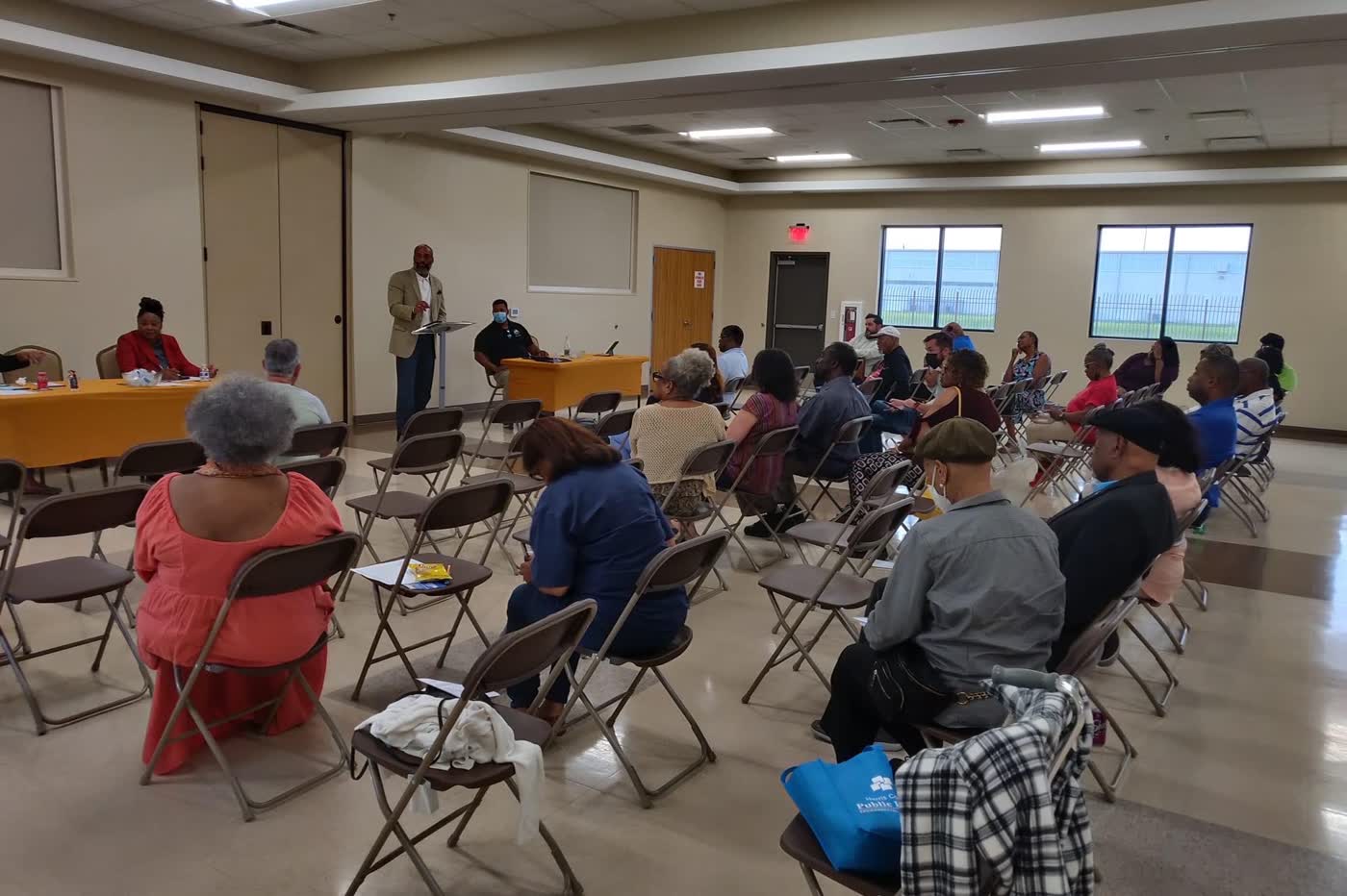 A community room of seated residents facing the front at a district meeting.