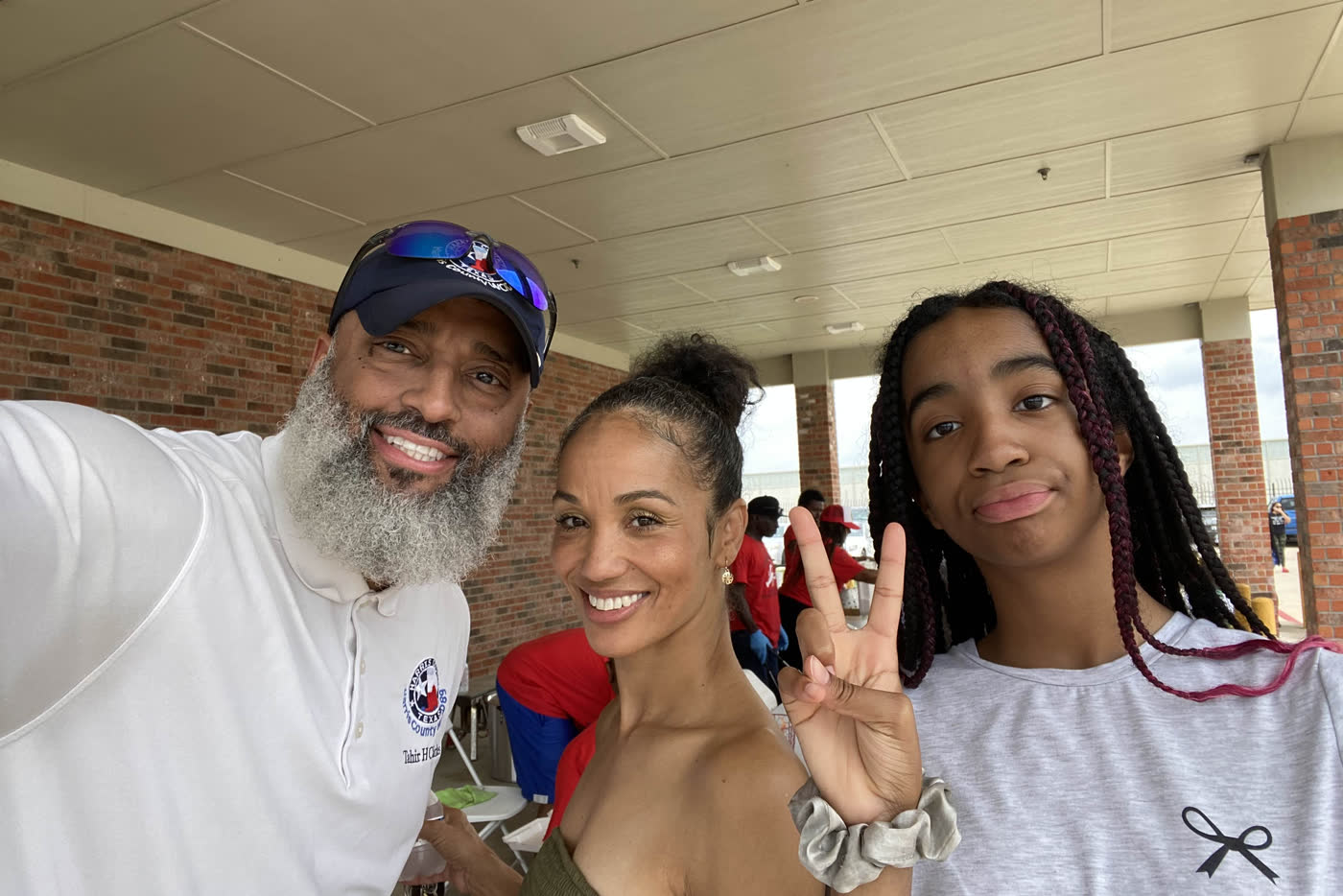 Tahir Charles taking a photograph with two residents under the covered drive at a district event.