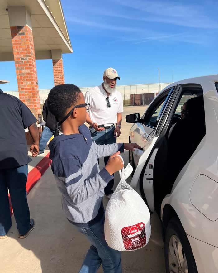 A young volunteer carrying a turkey to the open door of a waiting car while Tahir Charles looks on.