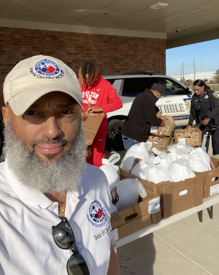 Tahir Charles in front of boxes of frozen turkeys being bagged by volunteers beside a constable vehicle.
